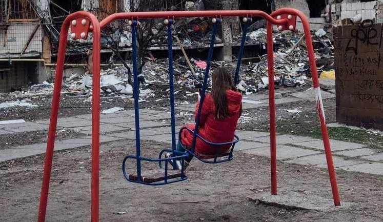 Дівчинка на дитячому майданчику біля зруйнованого російськими бомбами будинку. ФОТО ДНЯ