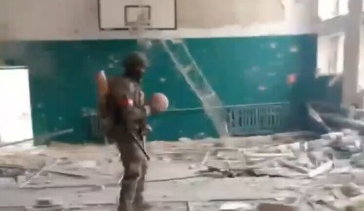 Occupiers play basketball among black bags with bodies of their accomplices in dilapidated gym. VIDEO