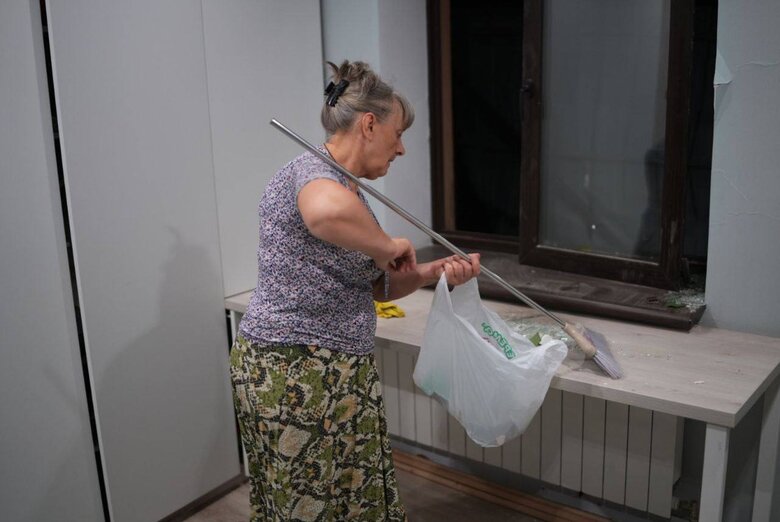 Жінка прибирає уламки вікна, яке вилетіло через вибух російського снаряду в Запоріжжі